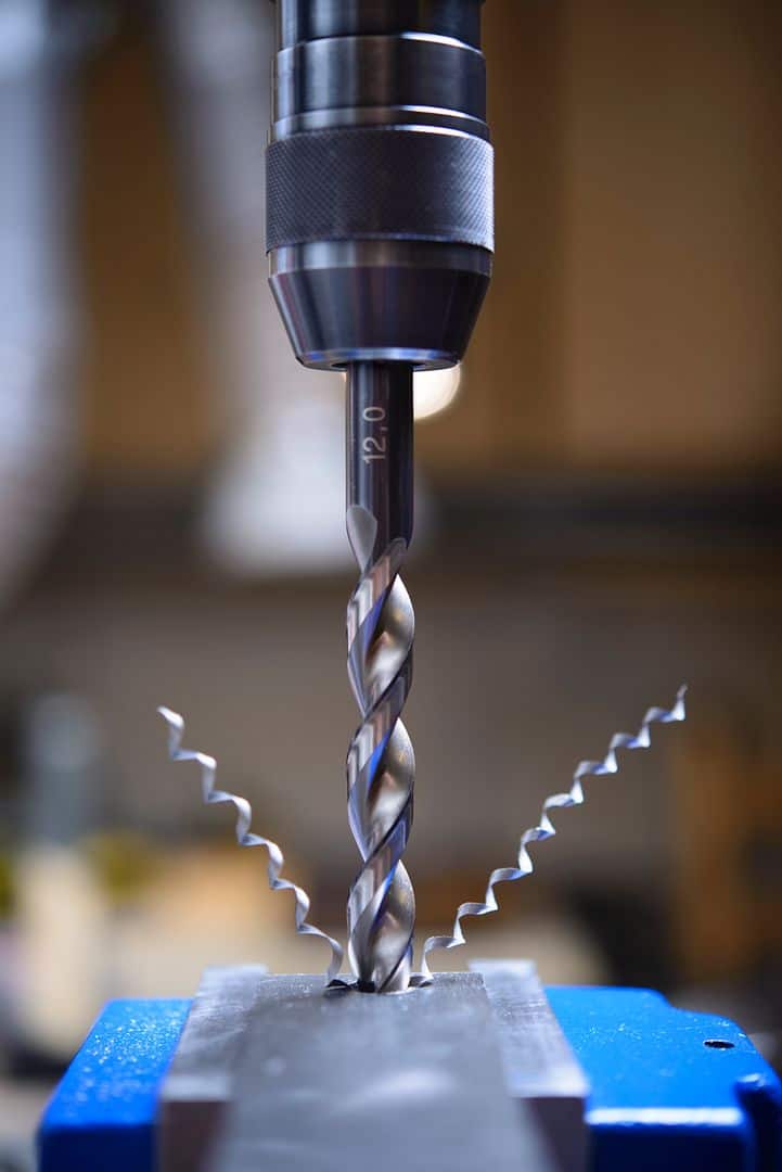Drill bit in a drill press close-up for industrial machining and manufacturing processes.