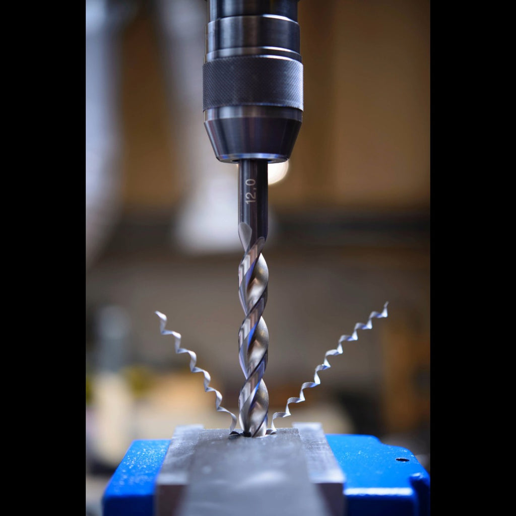 Precision drill bit cutting into metal secured in a blue vise, showcasing high-quality tools for industrial and mechanical machining.